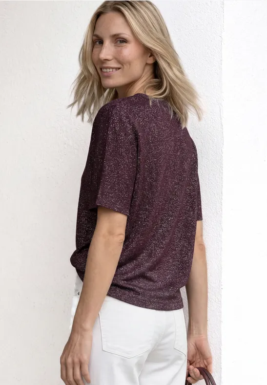Een persoon van achter gefotografeerd draagt een glitter T-shirt en witte jeans voor een witte achtergrond.