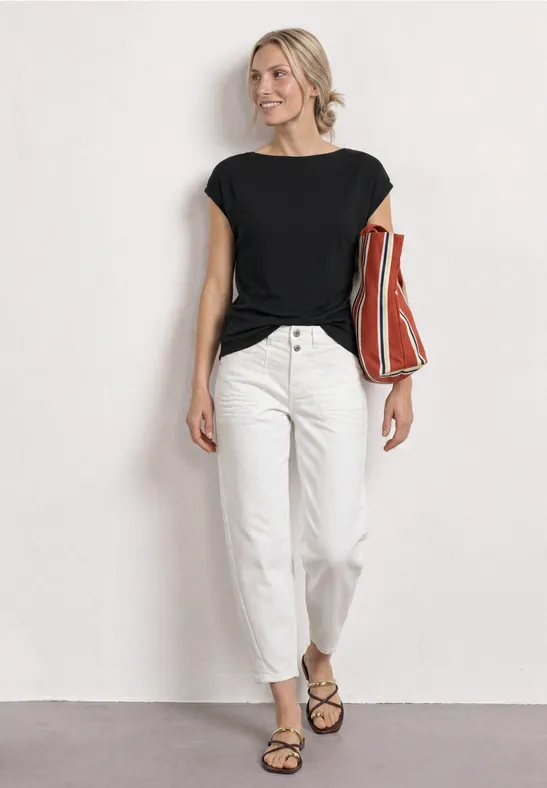 Person in schwarzem Shirt, weißer Hose und Sandalen mit rot-orange gestreifter Tasche vor weißem Hintergrund.