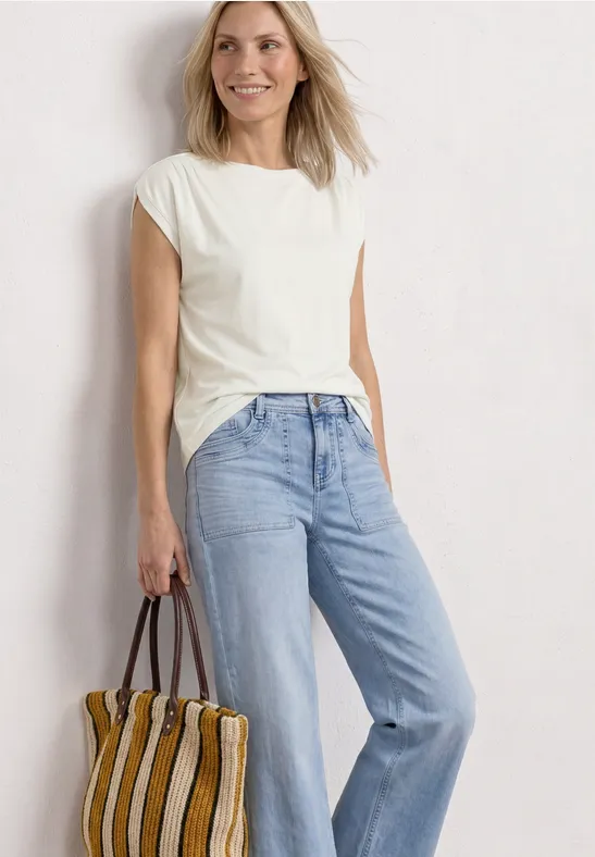 Frau mit weißem T-Shirt, hellblauer Jeans und gestreifter Tasche vor weißem Hintergrund.