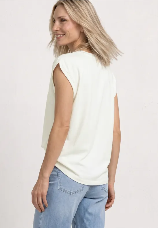 Eine Frau trägt eine weiße ärmellose Bluse und hellblaue Jeans, Rückansicht, Blick über die Schulter.