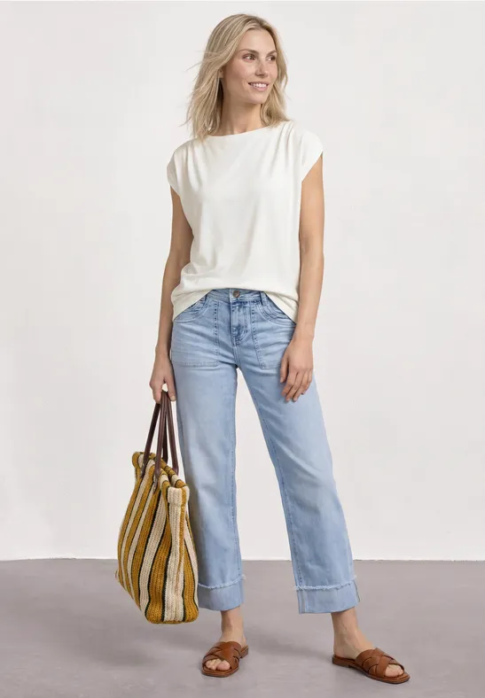 Frau in weißem T-Shirt, blauen, gerade geschnittenen Jeans und braunen Sandalen hält eine gelb-weiß gestreifte Tasche.