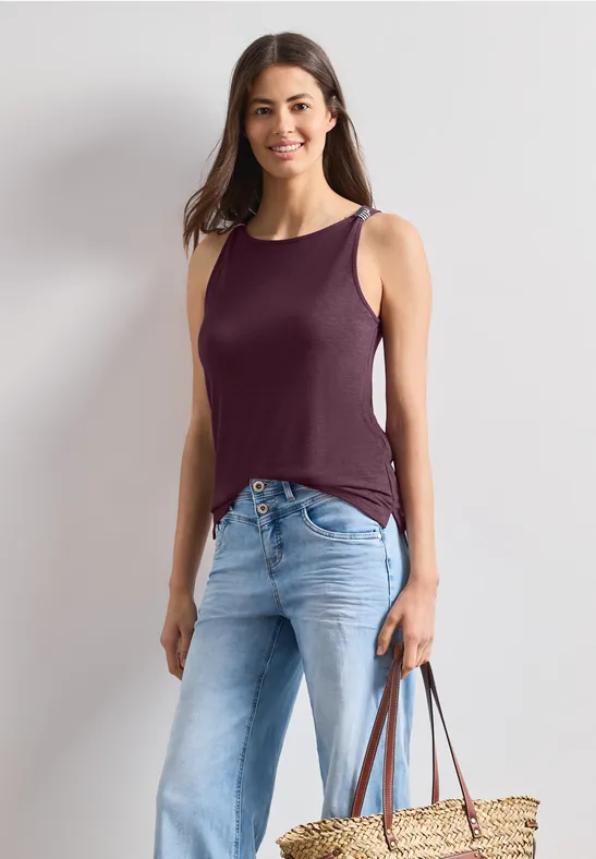 Vrouw in mouwloos paars topje en lichtblauwe jeans, met een strooien tas.