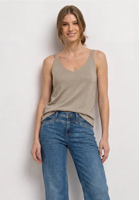 Vrouw in beige top en blauwe jeans voor een witte muur.