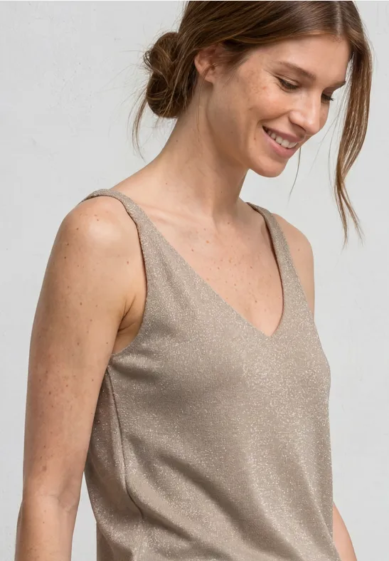 Vrouw met losse knot draagt glanzend beige topje met V-hals voor een lichte achtergrond.