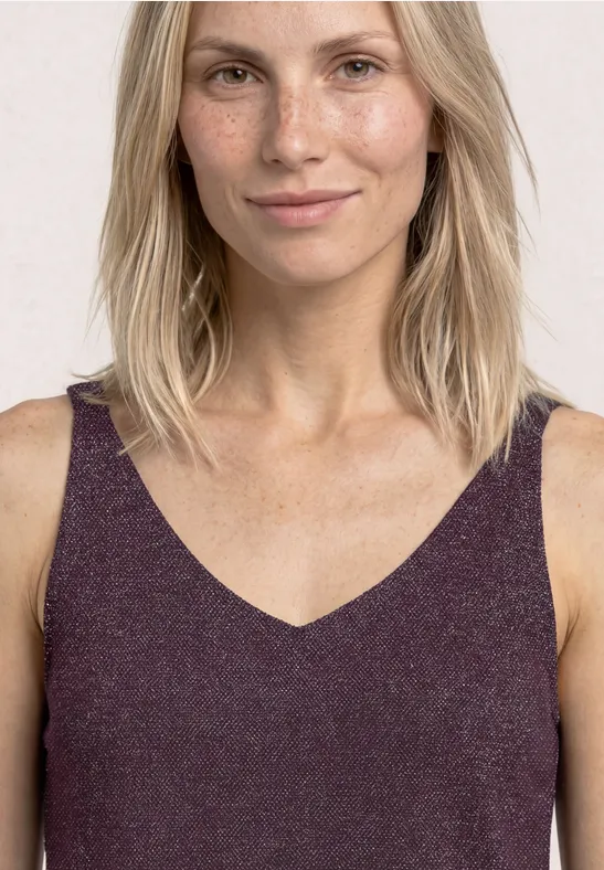 Vrouw met halflang blond haar in een mouwloos paars V-hals top voor een lichte achtergrond.