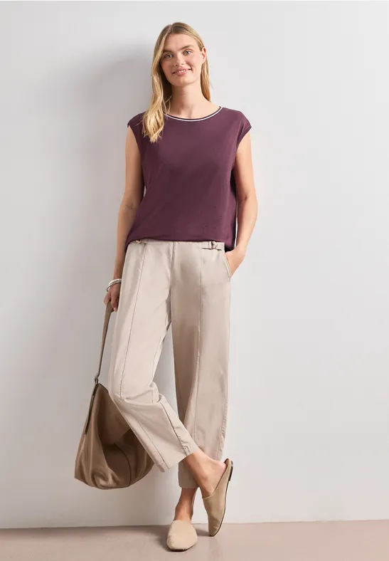 Vrouw in paars mouwloos topje, licht wijde broek, beige loafers en bijpassende tas.