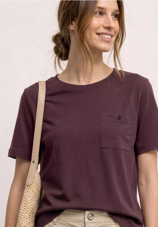 Vrouw in bordeaux t-shirt met borstzak en gevlochten schoudertas.