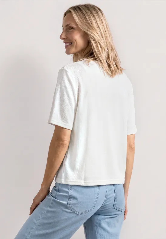 Frau mit blondem Haar in weißem T-Shirt und blauer Jeans, schaut von hinten.