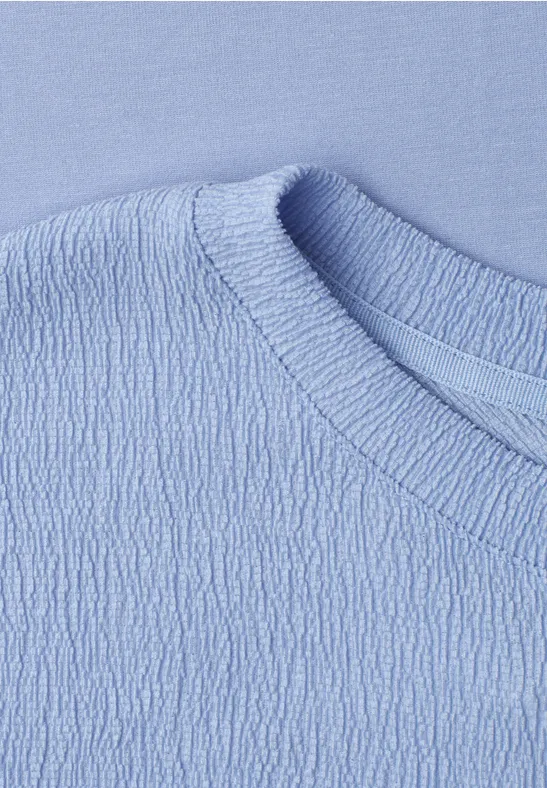 Gros plan d'un haut bleu ciel en tissu structuré avec col rond.
