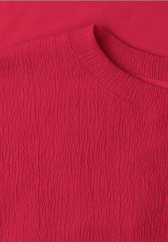 Close-up van een rood T-shirt met ronde hals en fijne, licht geribbelde textuur.