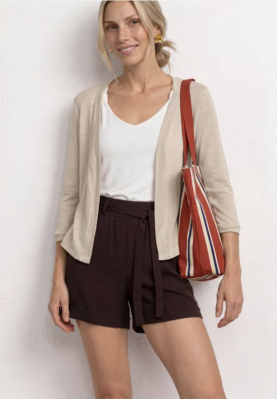 Femme avec un top blanc, un gilet beige, un short marron et un sac rayé.