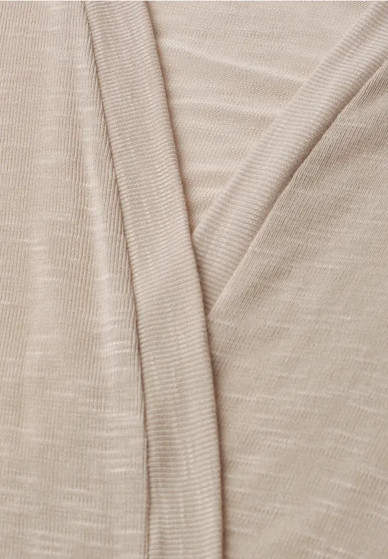 Gros plan d’un tissu beige finement tricoté, présentant un col en V et une texture délicate.
