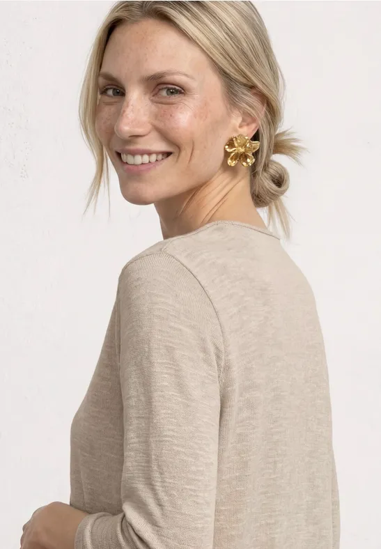 Vue de profil d'une femme en haut beige et boucles d'oreilles dorées en forme de fleurs, visage flouté.