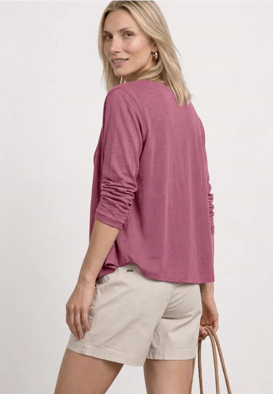 Vrouw van achteren in roze longsleeve en beige short, met een tas in de hand.