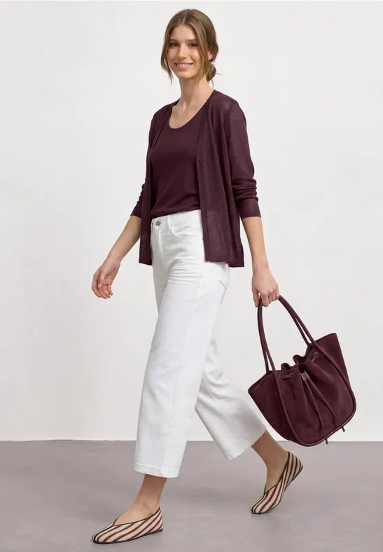 Femme en pull bordeaux, pantalon blanc, sandales zébrées et grand sac assorti.