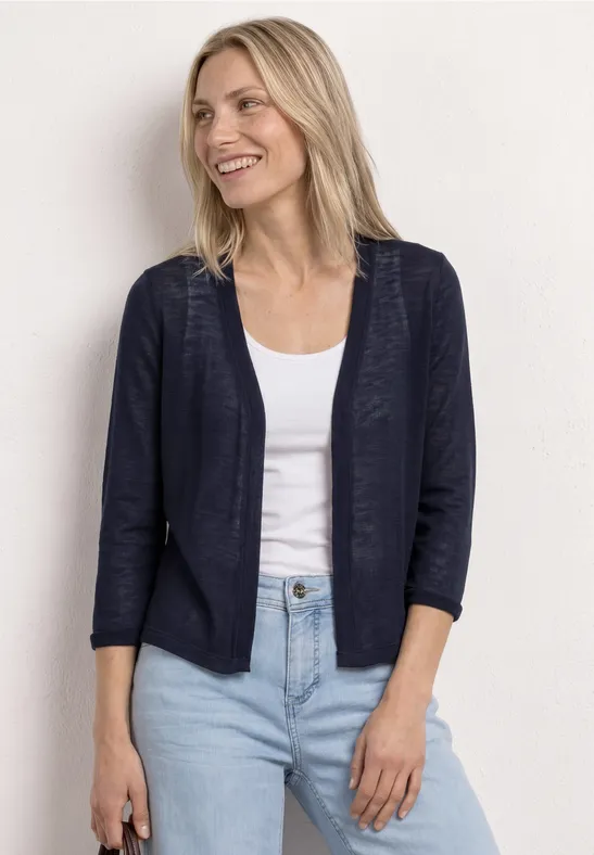 Femme portant un blazer bleu marine sur un débardeur blanc et un jean bleu clair devant un fond clair.