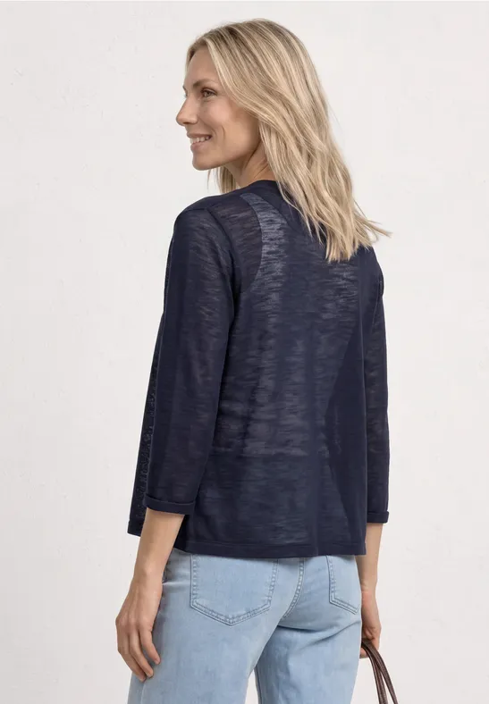 Femme de dos vêtue d'un gilet fin bleu marine à manches 3/4 et d'un jean clair, tenant un petit sac.