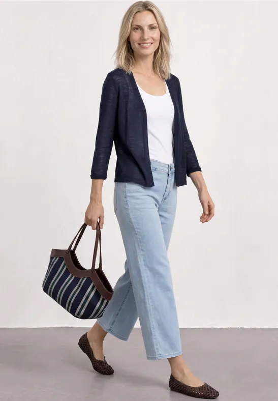 Femme en jean, t-shirt et blazer tenant un sac, sur fond neutre.