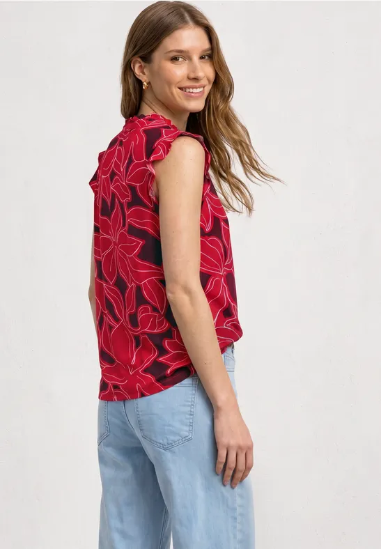 Een vrouw in zijaanzicht draagt een rood mouwloos top met bloemenprint en een lichtblauwe spijkerbroek.