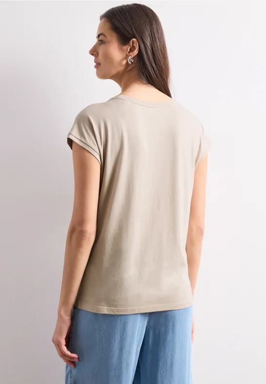 Vrouw van achteren in beige T-shirt met korte mouwen en wijde blauwe jeans, neutrale achtergrond.