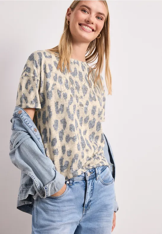 Vrouw in luipaardprint T-shirt en lichte jeans, met spijkerjasje nonchalant over de schouder.