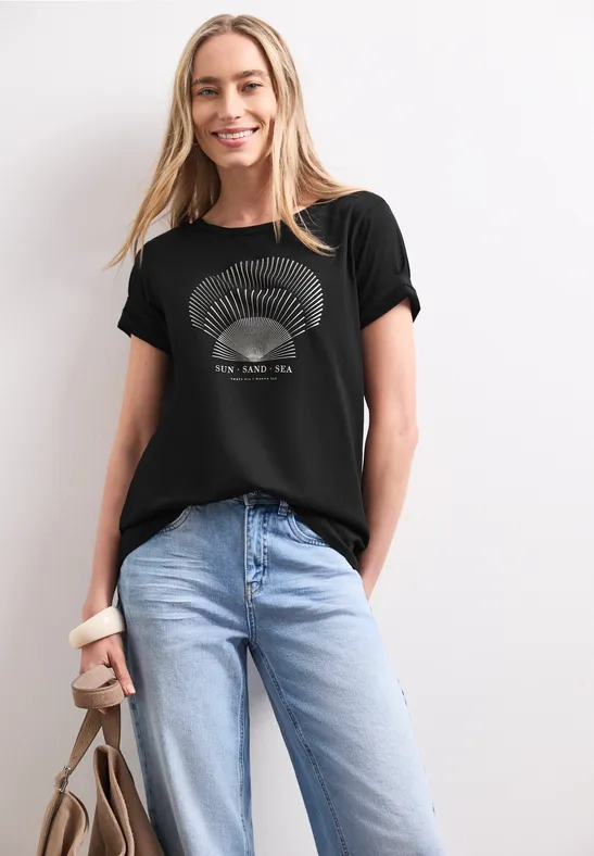Frau trägt schwarzen Print-T-Shirt, blaue Jeans und hält eine braune Tasche.