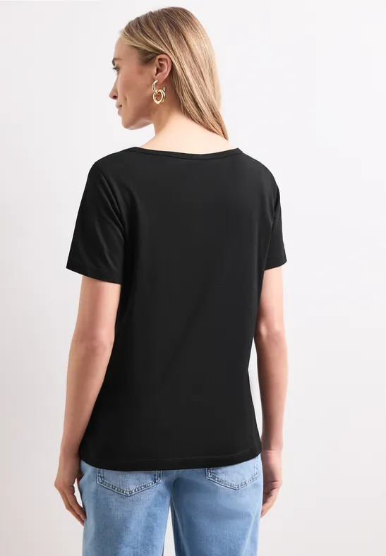 Rückansicht einer Frau mit schwarzem T-Shirt und blonden Haaren, die blaue Jeans trägt.