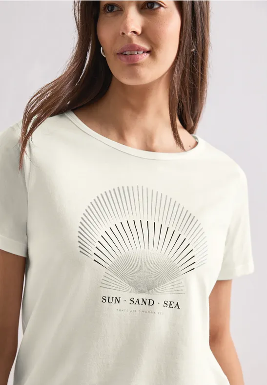 Frau trägt helles T-Shirt mit Sonnen- und Meeresmotiv und Schriftzug 'SUN SAND SEA'.