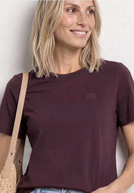 Een glimlachende vrouw in een kastanjebruin T-shirt met een beige tas tegen een lichte achtergrond.