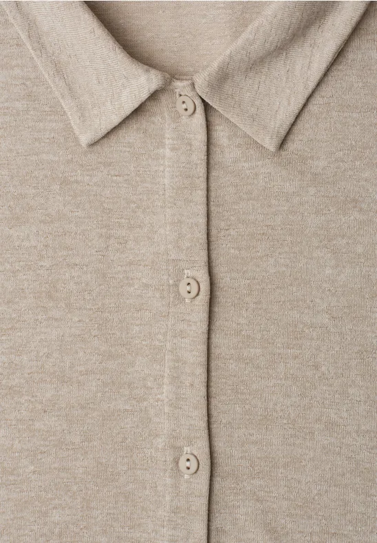 Close-up van een beige gebreid vest met overhemdkraag en knopenrij.