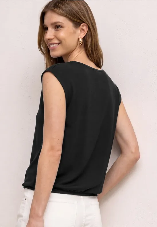 Een vrouw van achteren in een zwart mouwloos topje en witte broek.