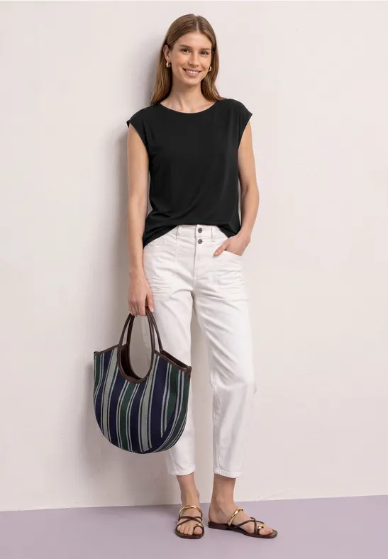 Vrouw in zwarte top, witte spijkerbroek en sandalen met een gestreepte tas.