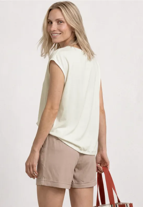 Vrouw van achteren in roomwit shirt en beige short, met rode tas.