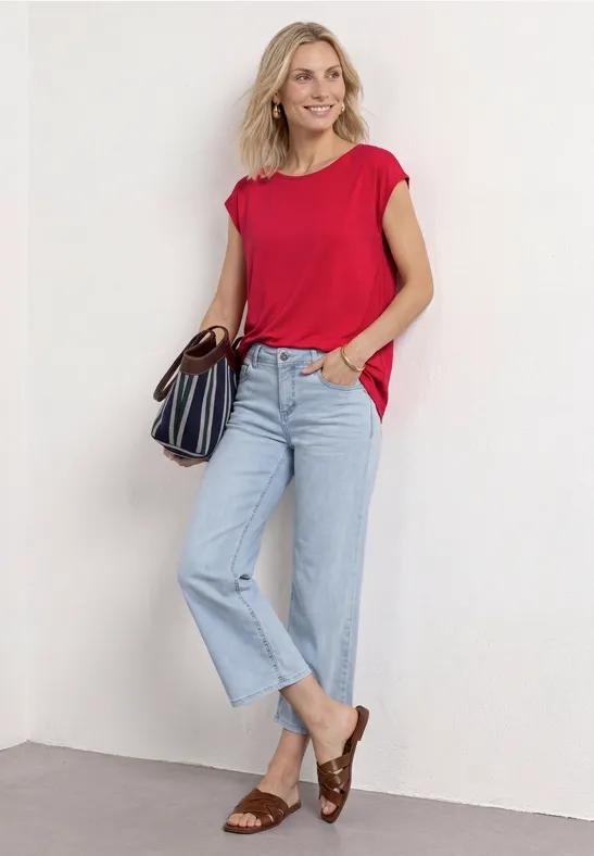 Vrouw in rood T-shirt, lichtblauwe jeans en bruine sandalen met een gestreepte handtas.