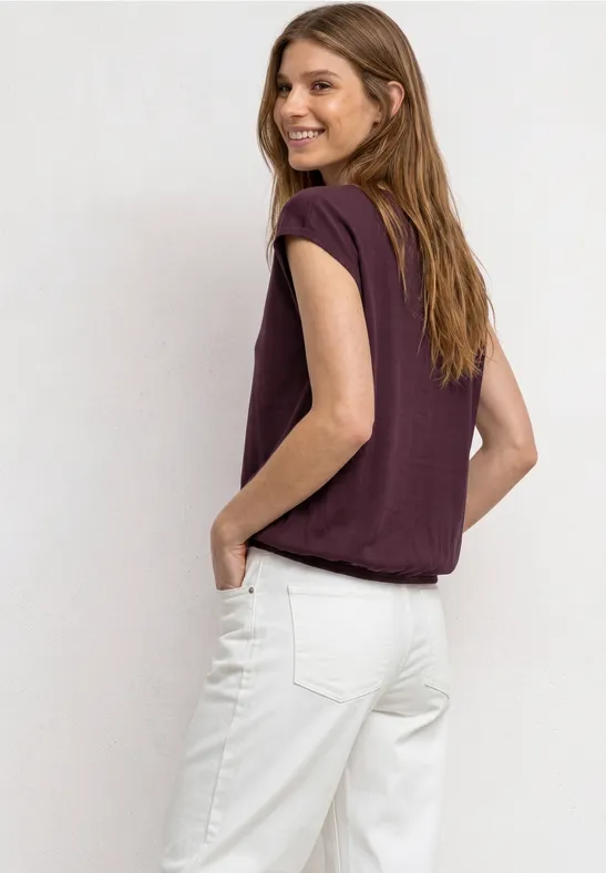 Van achteren gefotografeerde vrouw in paarse t-shirt en witte jeans.