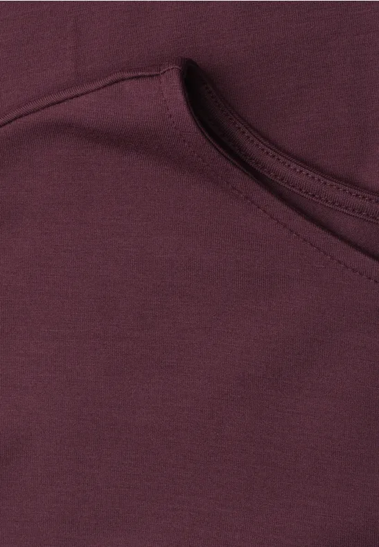 Close-up van een bordeauxrode capuchontrui met zichtbare zak en stikseldetails.