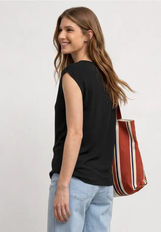Eine Frau von hinten in schwarzem ärmellosen Top, hellen Jeans und einer rot-weiß gestreiften Tasche.