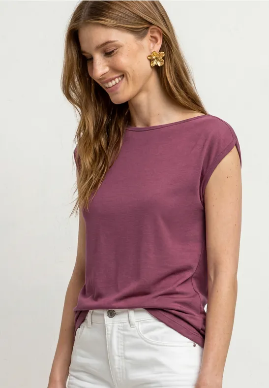 Een vrouw draagt een paarse T-shirt en een witte broek.