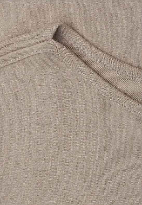 Close-up van een lichtbeige T-shirt met zichtbare stiknaad bij de halslijn.