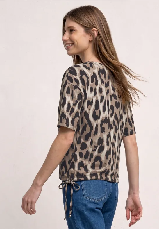 Vrouw in jeans en shirt met korte mouwen en luipaardprint, driekwartaanzicht van achteren.