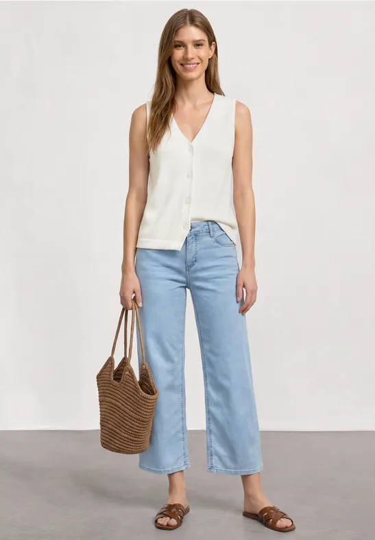 Frau in weißer ärmelloser Bluse, weitem hellblauem Jeans, braunen Sandalen und geflochtener Tasche.