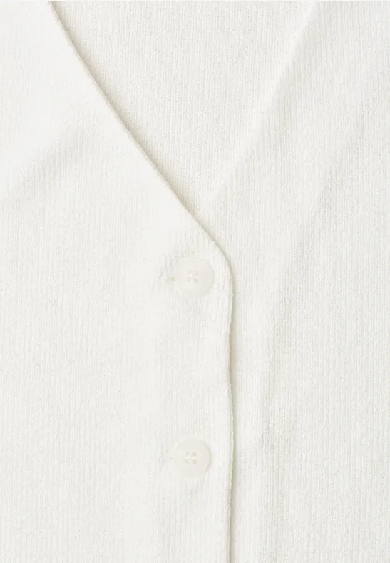 Nahaufnahme eines weißen Strickcardigans mit V-Ausschnitt und zwei Knöpfen.