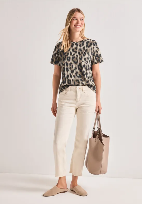 Frau in Leoparden-Print-T-Shirt, heller Cropped-Hose, beigen Slippern und einer passenden Tasche.
