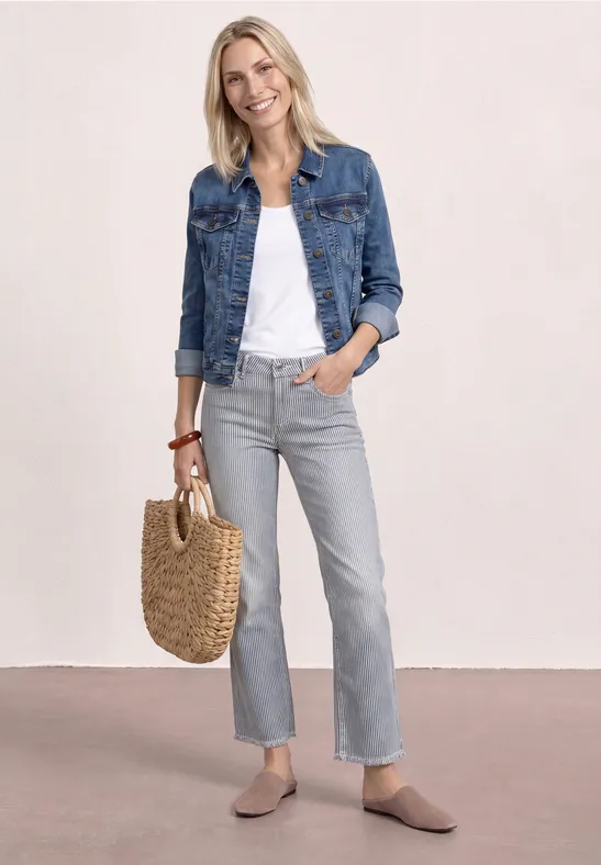 Vrouw met spijkerjas, wit topje, grijze jeans, beige instappers en een rieten tas.