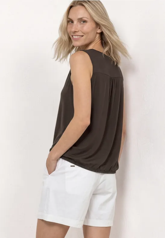 Vrouw van achteren in zwart mouwloos topje en witte korte broek, handen in de zak.
