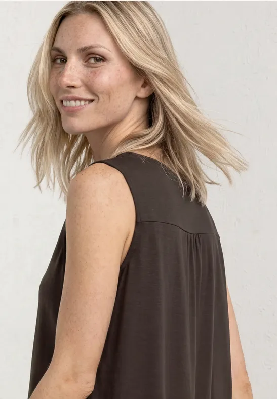 Vrouw met schouderlang blond haar, draagt een zwart mouwloos topje en kijkt opzij.