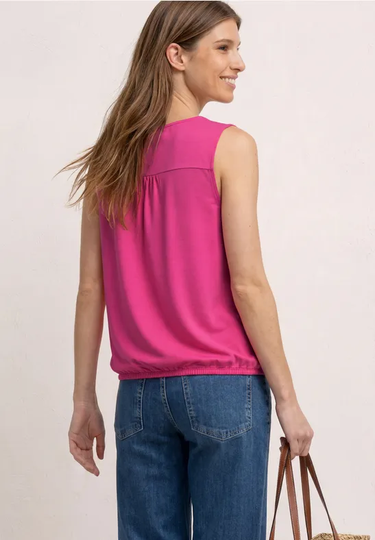 Frau von hinten in pinkem, ärmellosem Top, Jeans und brauner Tasche vor hellem Hintergrund.