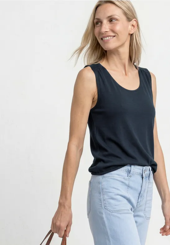 Femme en débardeur noir et jean bleu clair, tenant un sac à la main.