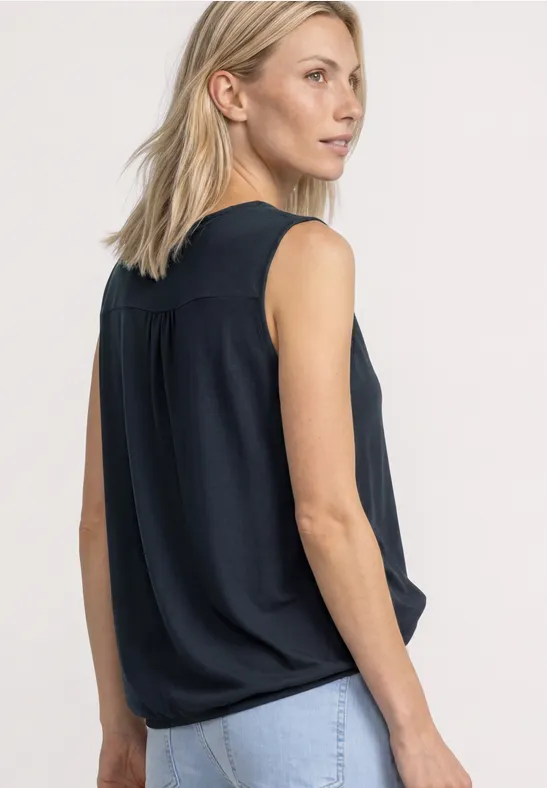Une femme blonde vue de dos, portant un top sans manches bleu foncé et un jean bleu clair.