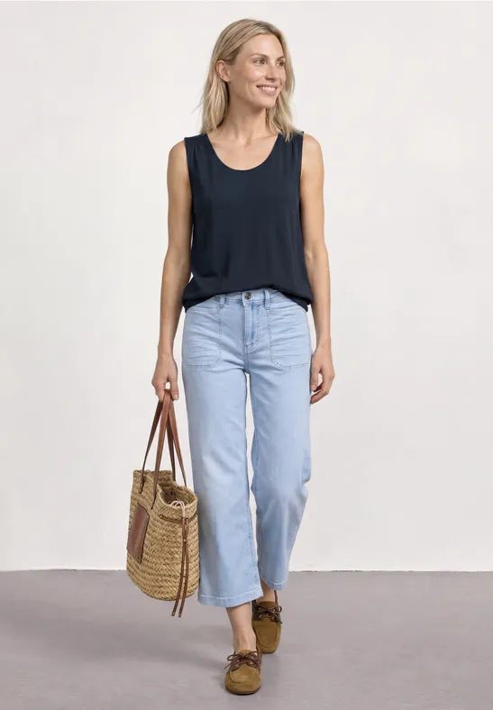 Femme en top noir, jean bleu clair et mocassins marron, portant un sac tressé sur fond clair.